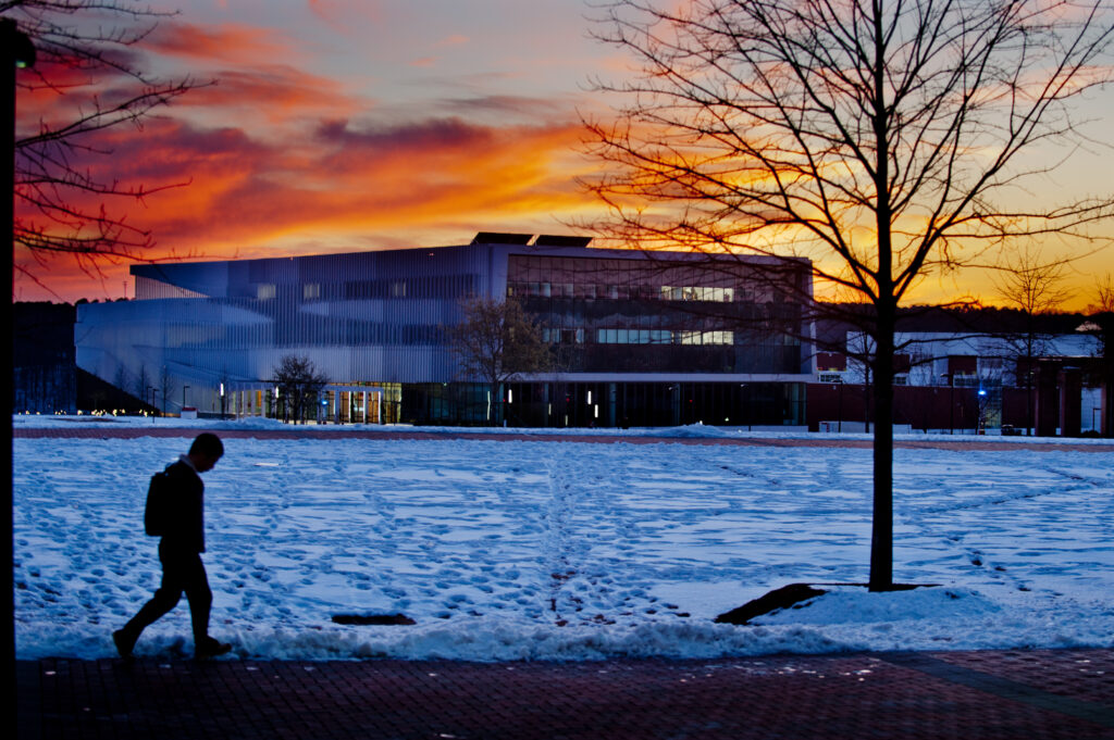 Walking through snow in front of building at sunset